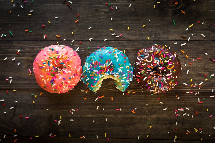 3 donuts in a row on a table, with sprinkles covering them. the donut in the centre has had a bite taken from it.