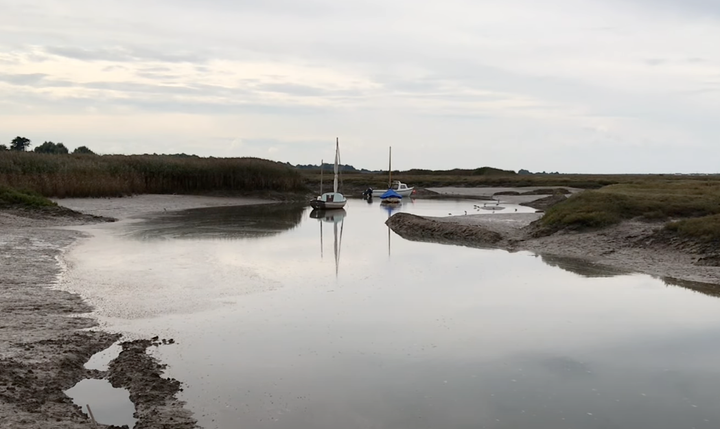 photo of Brancaster Staithe showing part of the estuary and two small sailing boats anchored in the distance