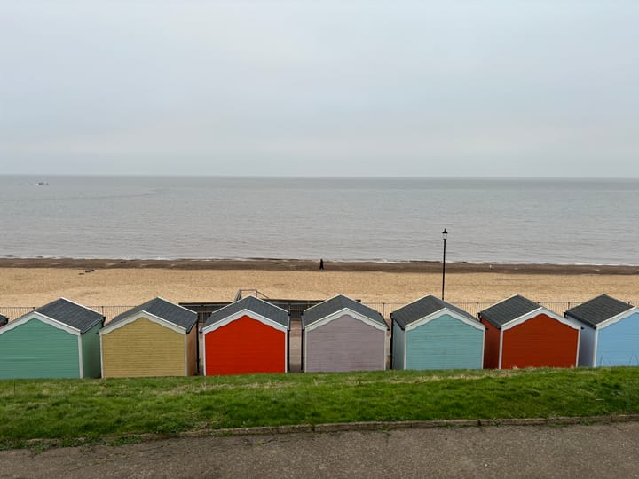 Row of coloured beach huts in the foreground, beach in the middle distance and sea in the background